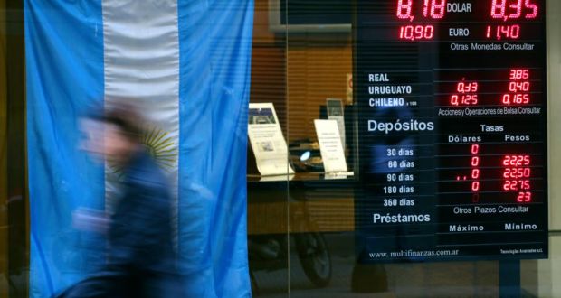 A woman walks past a currency exchange store with an Argentine national flag on display in