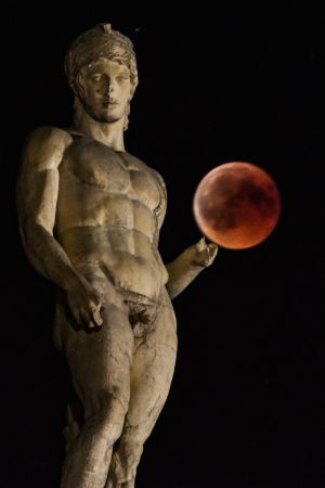   The eclipsed moon is shown next to a statue of the ancient Greek god Ares in central Athens. Photo: AFP PHOTO / Aris MESSINISARIS MESSINIS / AFP / Getty Images

