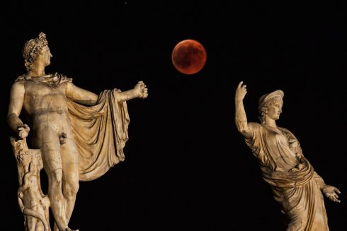   The moon appears next to a statue of the ancient Greek gods Hera (R) and god Apollo in the center of Athens. Photography: Aris MESSINISARIS MESSINIS / AFP / Getty Images
