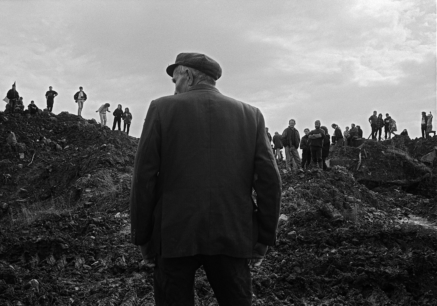 An old man inspects a large earth bank straddled by people of all ages marking the Irish Border