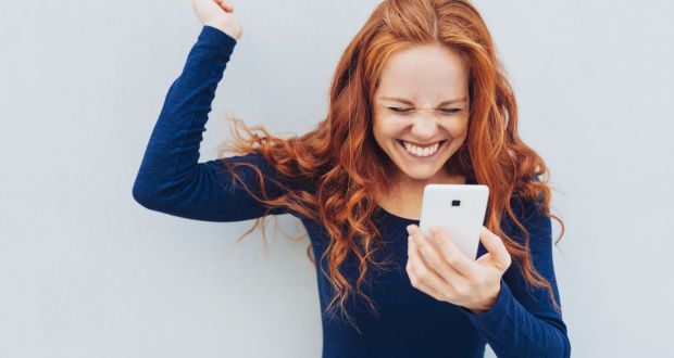 Young redhead celebrating good news on her mobile phone cheering and raising her fist in exultation