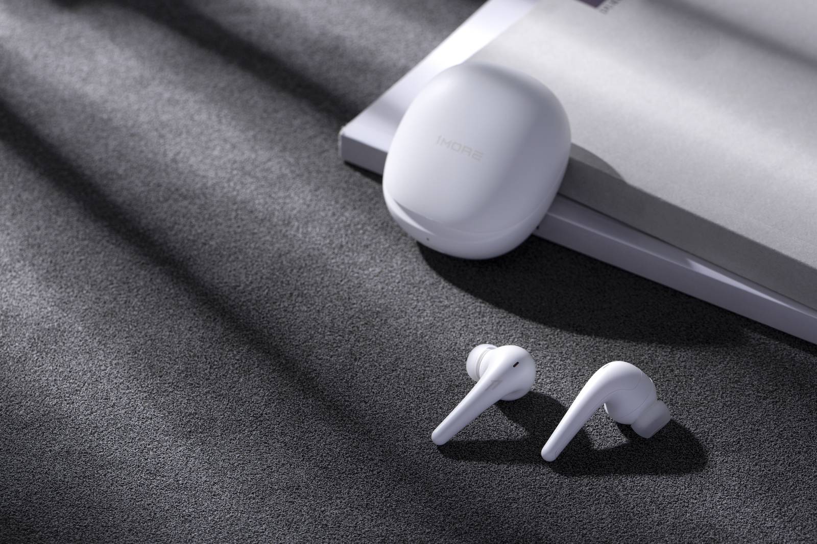 two white earbuds and a pebble shaped case sitting against a laptop