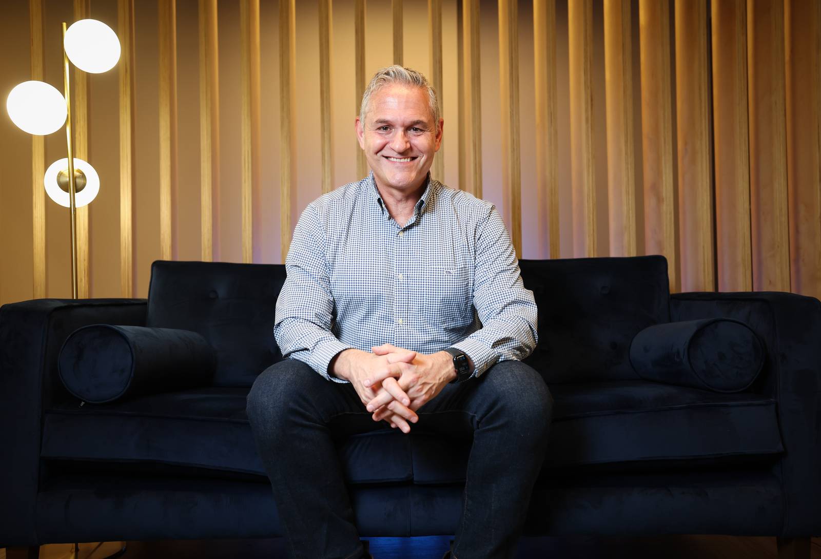 Cloudsmith chief executive Glenn Weinstein, smiling while sitting on a dark sofa.