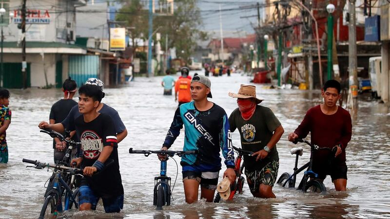 Filipino villagers wade along a flooded road in  Nabua. Photograph: EPA