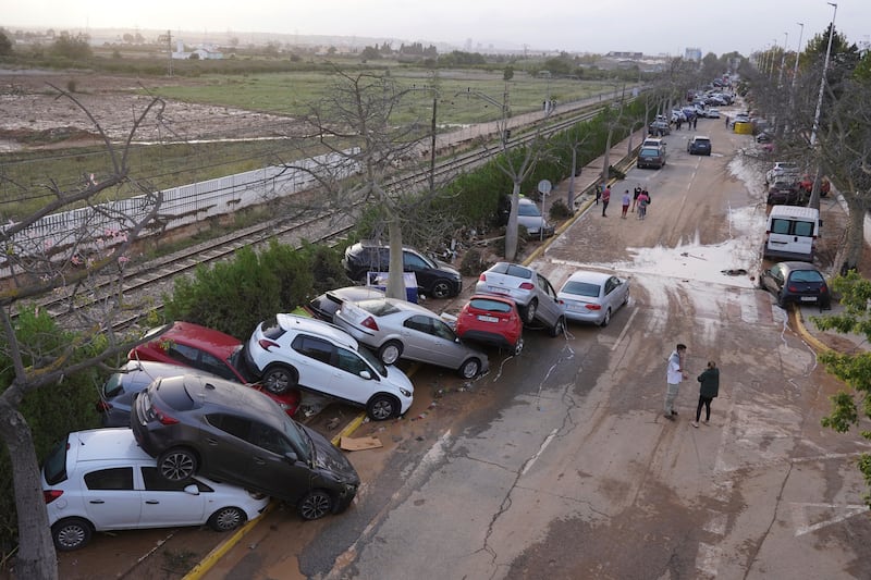 Residents walk next to cars piled up after being swept away by floods in Paiporta. Photograph: Alberto Saiz/AP