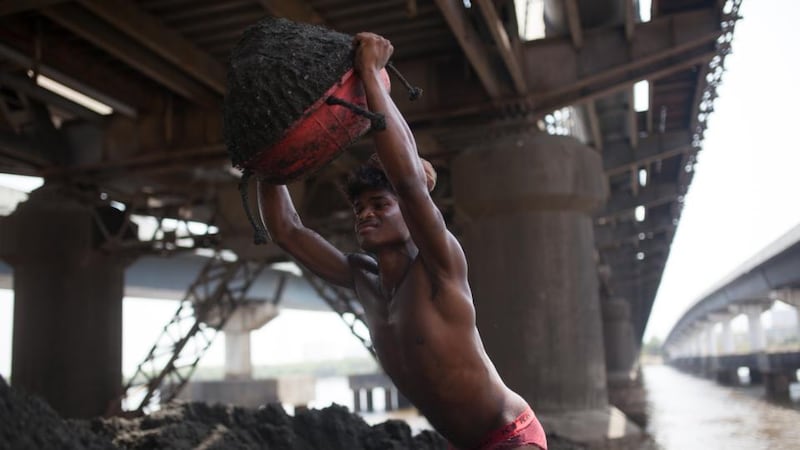 A worker empties sand mined from the Vasai Creek bed on the shore in Bhiwandi, Thane, India. Photograph: Thomson Reuters Foundation