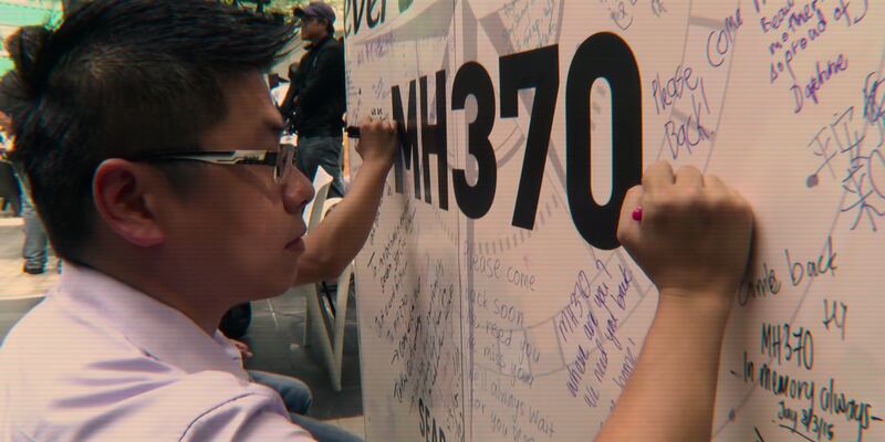 A man writes a message on a commemorative display for the people onboard flight MH370. 