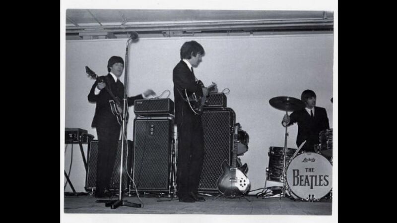 The Beatles play live in the King’s Hall in south Belfast in November 1964. Left to right are Paul McCartney, George Harrison and Ringo Starr, with John Lennon out of shot. The shot shows classic 1960s instruments awaiting play including a Rickenbacker electric guitar and a Vox Continental electric organ at left.  File photograph: Nick Newbery/PRONI