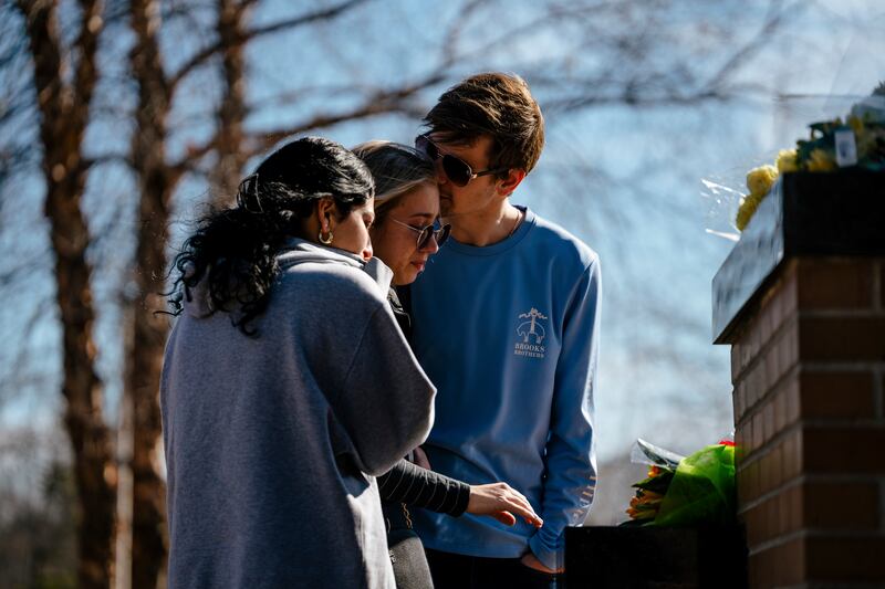 Katy James, Jillian Isaac, and Traxel Jirgens leave flowers under a statue on the Michigan State University campus. Photograph: Nick Hagen/The New York Times)