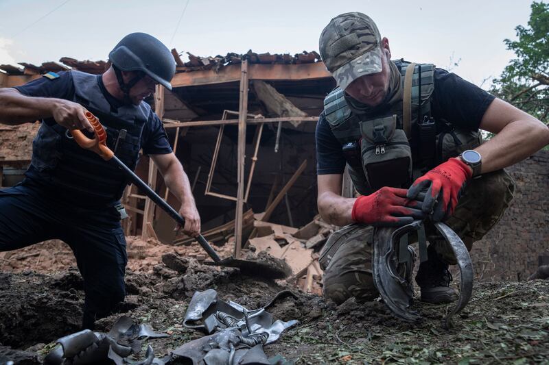 A policeman, right, inspects a piece of a rocket after a Russian bombardment at a residential neighbourhood in Kharkiv (Evgeniy Maloletka/AP)