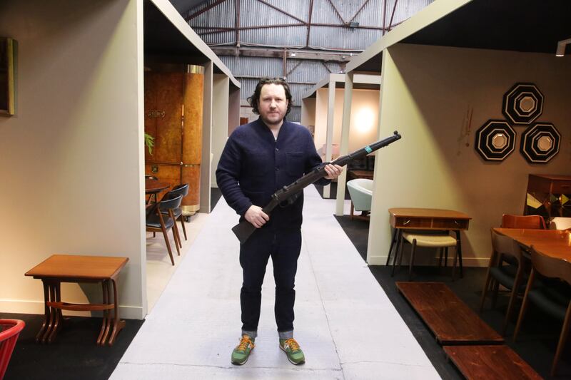 Killian McNulty of Historic Interiors with a prop rifle used in the 1996 film Michael Collins, set priced at €300-€500, which will feature in the Historic Interiors online auction valued at €400,000 from December 5-8. See irishcountryhome.com for more. Image credit: Niall Mullen.