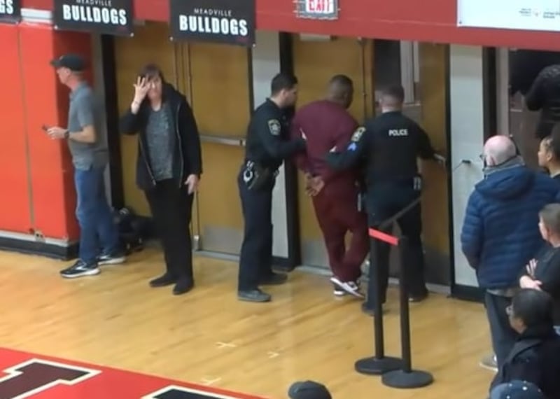 A man is led away in handcuffs by the police as the Meadville versus Uniontown basketball game ended in a brawl