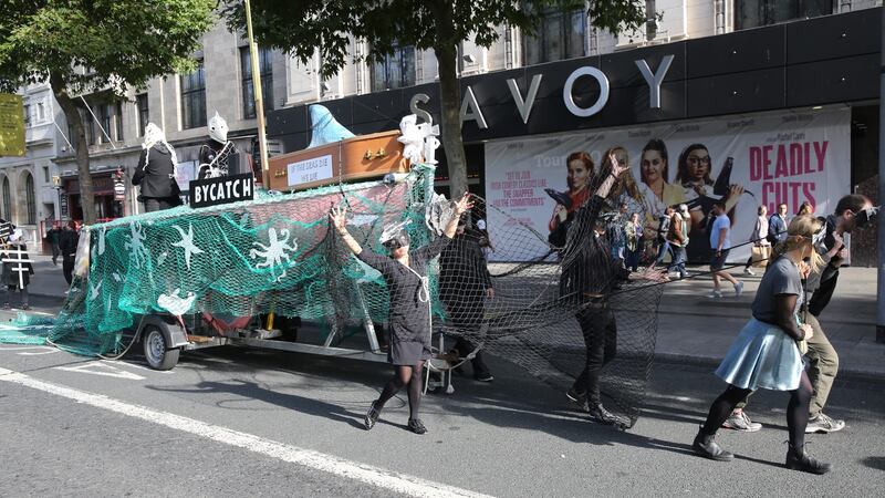 A trawler, which contains  a wooden coffin stating, ‘If the seas die we die’, is pulled along the streets by activists dressed as dead fish in skeletal masks.  Photograph: Gareth Chaney/Collins