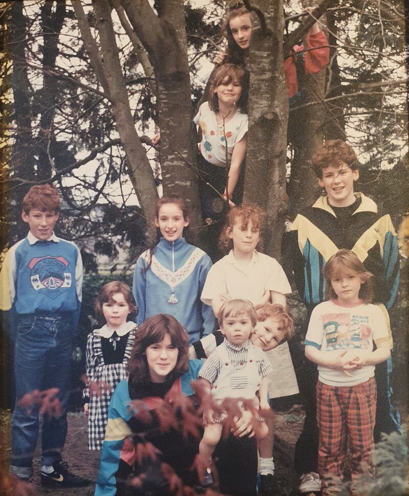 1990: Maeve (in tree), and Dearbhaile below her. Standing: Shane, Fionnuala, Orla, Mairead and Dara. Front: Sinead, with Conall on her hip, and Séamas poking over Conall’s shoulder