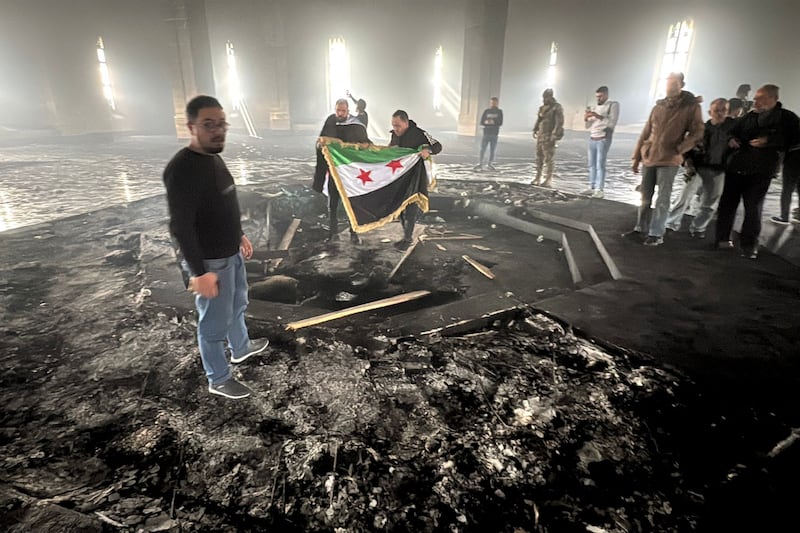 Rebel fighters stand with the flag of the revolution on the burnt gravesite of Syria's late president Hafez al-Assad at his mausoleum in the family's ancestral village of Qardaha in the western Latakia province on Wednesday. Photograph: Aaref Watad/AFP via Getty Images