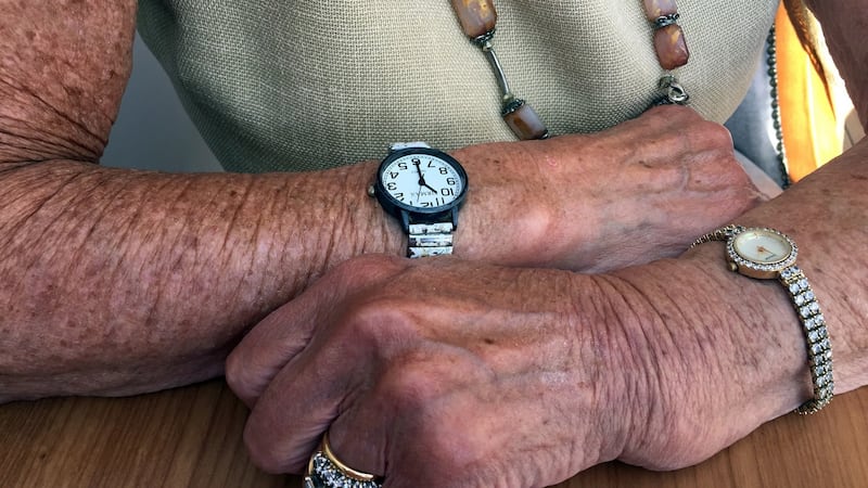 Rosie, age 88, is tanned from sunbathing in her front garden. She wears two watches. Her late husband gave her the jewelled watch and rings. Her daughter gave her the other watch, with large numerals so she can read the time