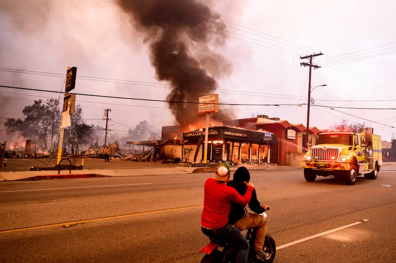 Residents ride their motorbike past a burning liquor store in the Altadena area of Los Angeles county. Photograph: Josh Edelson/AFP