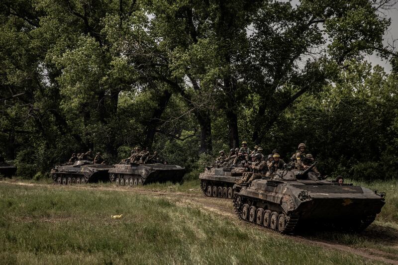 A column of Ukrainian armored vehicles and soldiers travel under the cover of a tree line near the front lines in the Donetsk region of Ukraine