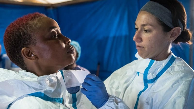 Love Fassama, a Liberian nurse assistant, is helped by Bridget Anne Mulrooney, a volunteer nurse from the US, into protective clothing before a shift at a clinic run by the International Medical Corps in Suakoko, Liberia. Photograph: Daniel Berehulak/The New York Times