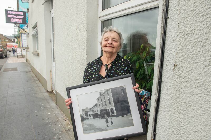 Margaret Kelleher in front of her old home on Market Quay, Youghal, with a black-and-white framed photo of how it looked during filming of Moby Dick 69 years ago. Photograph: Michael Mac Sweeney/Provision