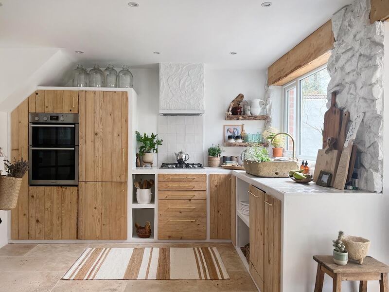 An upcycled kitchen designed by Peter Irvine of Peter Irvine Design. He achieved this look on a budget by using free pallet wood for the doors, paying £180 for his sink, which was a salvaged trough planter, making the dining table from scaffolding boards, paying just £20 for the vintage train station benches, and getting the stone walls, the 100 year old larder cabinet, the kitchen door and side stool from friends and family. 