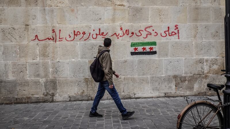 In Damascus old city, a man walks past graffiti which reads 'Best souvenir forever: f*ck you Assad'