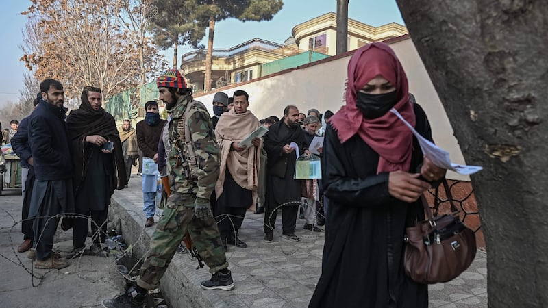 A Taliban fighter walks past people waiting to enter the passport office at a checkpoint in Kabul on Sunday, after Afghanistan’s Taliban authorities said they will resume issuing passports. Photograph:  Mohd Rasfan/AFP via Getty Images