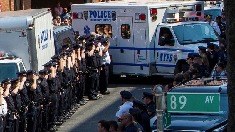 Lines of police officers salute as an New York Police Department  ambulance carries  the body of  Brian Moore, who died Monday from injuries received when he was shot on Saturday, at Jamaica Hospital Medical Center in New York on Monday evening.