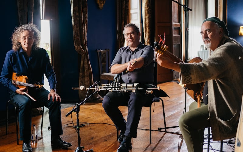 L-R: Martin Hayes, seated with fiddle under right arm, with David Power, with pipes on his lap and arms folded, and Steve Cooney, with his arms resting on his guitar